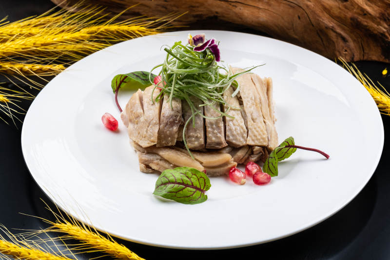 圆形瓷盘装的白斩鸡摆放在黑色背景上图片