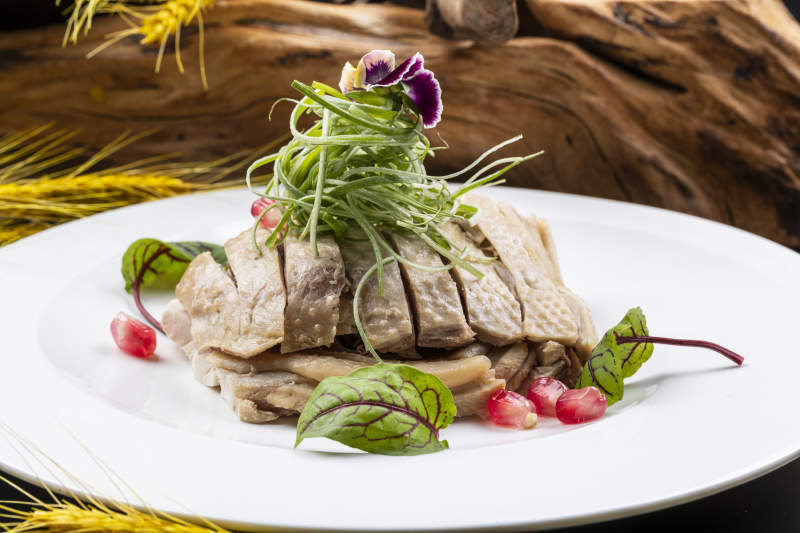 圆形瓷盘装的白斩鸡摆放在黑色背景上图片