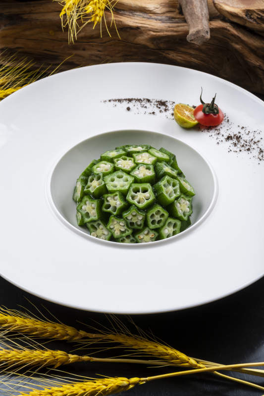 圆形瓷盘装的捞汁鲜秋葵摆放在黑色背景上图片