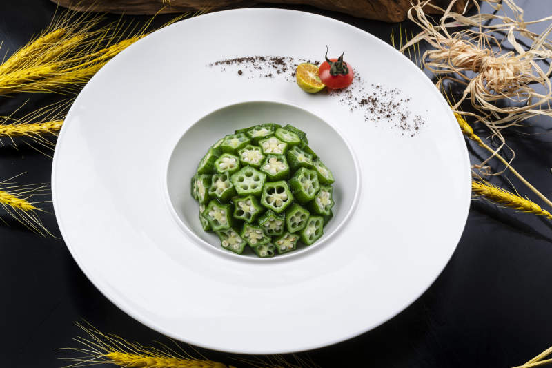 圆形瓷盘装的捞汁鲜秋葵摆放在黑色背景上图片