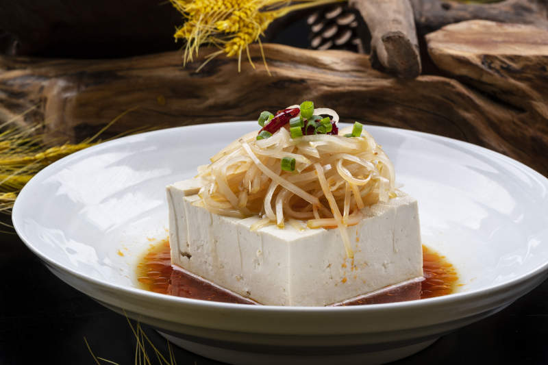 圆形瓷盘装的一品豆腐摆放在黑色背景上图片