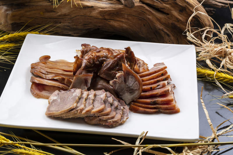 方形瓷盘装的卤肉拼盘摆放在黑色背景上图片