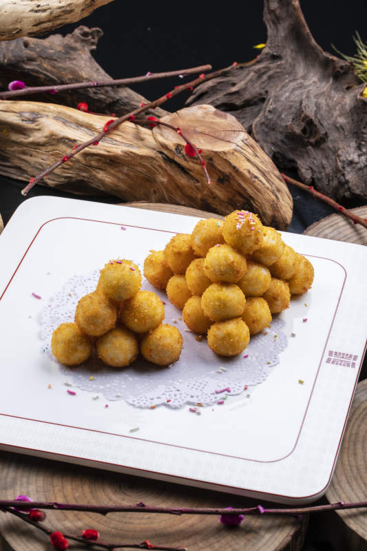 方形瓷盘装的黄金炸汤圆摆放在樟木砧板上图片