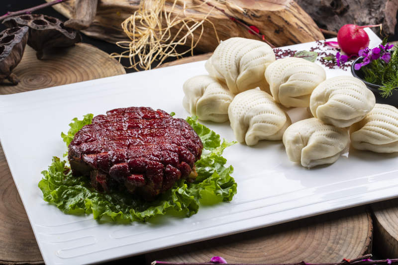 长方形瓷盘装的花馍夹酱肉摆放在樟木砧板上图片