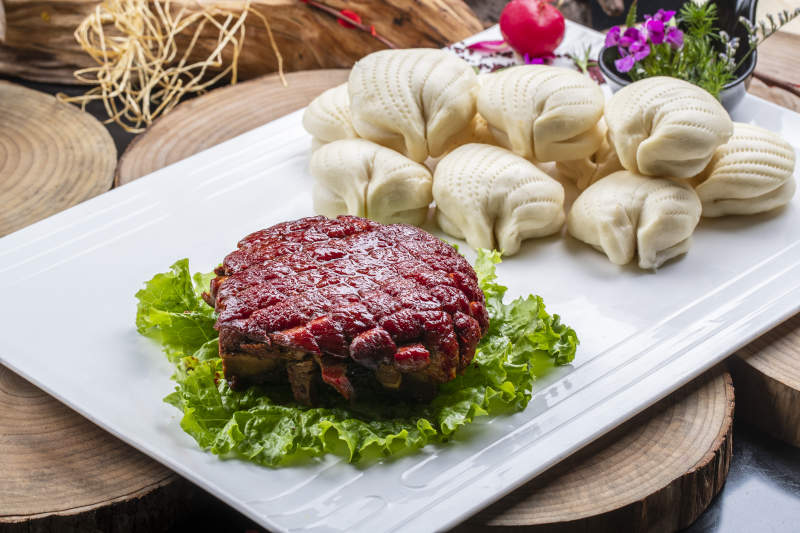 长方形瓷盘装的花馍夹酱肉摆放在樟木砧板上图片