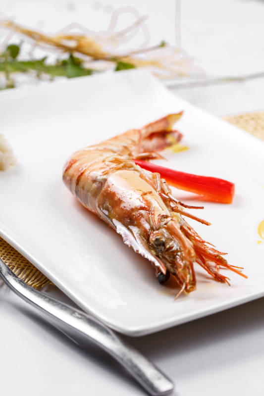 长方形瓷盘装的铁板野生明虾皇摆放在草垫上图片