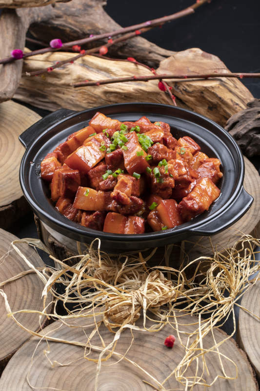 黑色砂锅装的锅仔红烧肉摆放在樟木砧板上图片