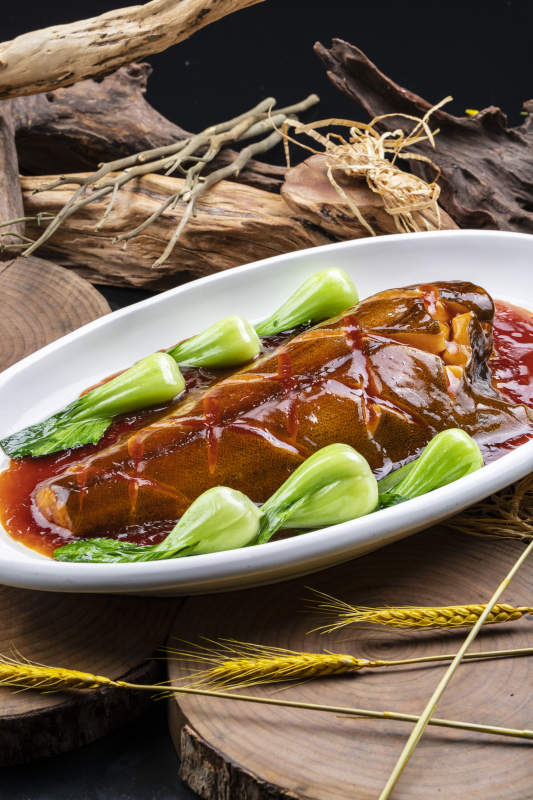 椭圆瓷盘装的红烧鲽鱼尾摆放在樟木砧板上图片