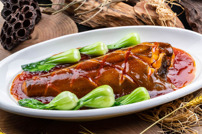 椭圆瓷盘装的红烧鲽鱼尾摆放在樟木砧板上图片