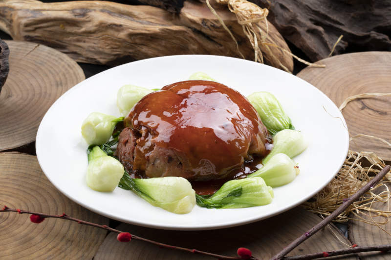 圆形瓷盘装的红焖扣肉摆放在樟木砧板上图片