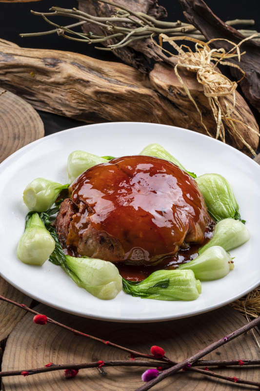 圆形瓷盘装的红焖扣肉摆放在樟木砧板上图片