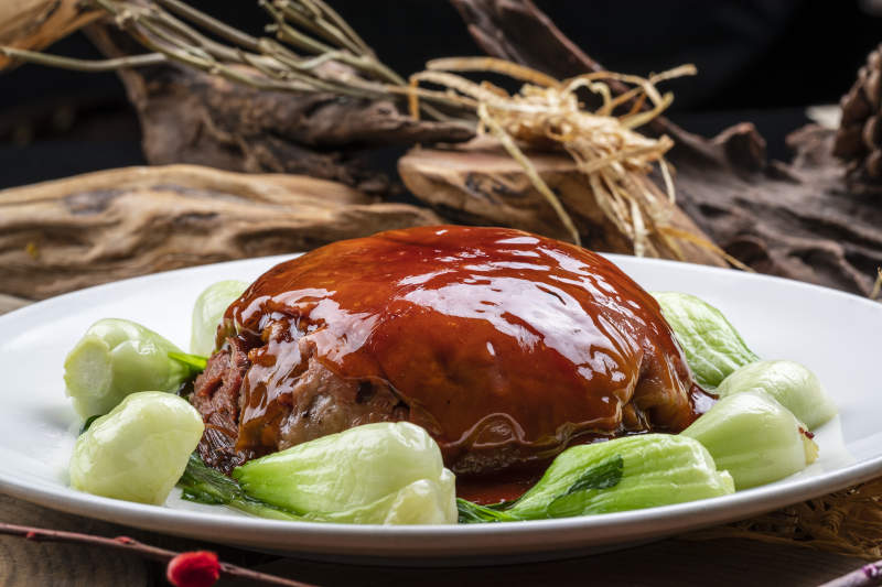 圆形瓷盘装的红焖扣肉摆放在樟木砧板上图片