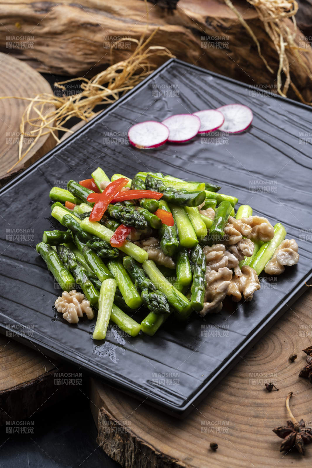 黑色石盘装的鲜芦笋桃仁摆放在樟木砧板上图片