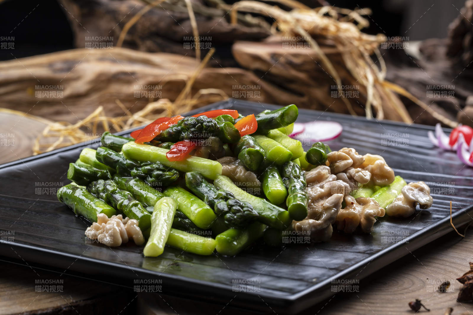 黑色石盘装的鲜芦笋桃仁摆放在樟木砧板上图片