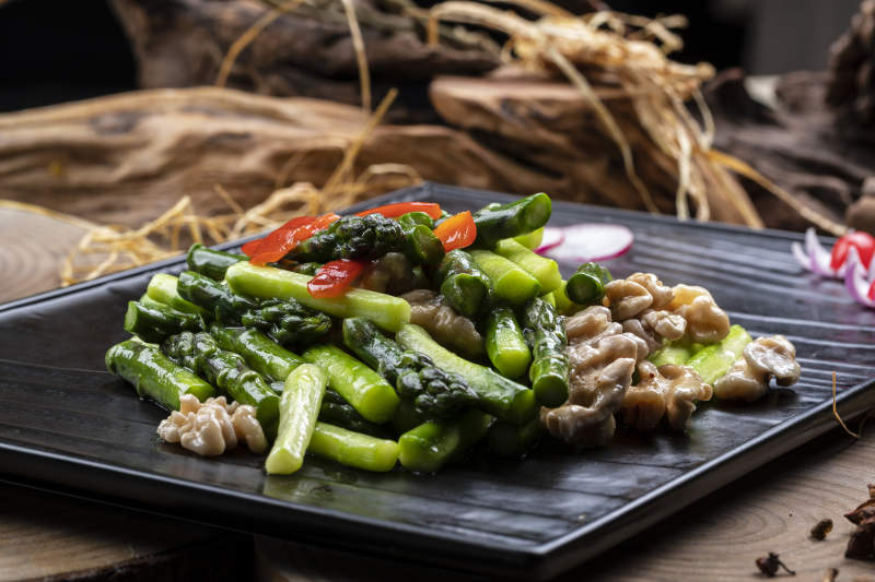 黑色石盘装的鲜芦笋桃仁摆放在樟木砧板上图片