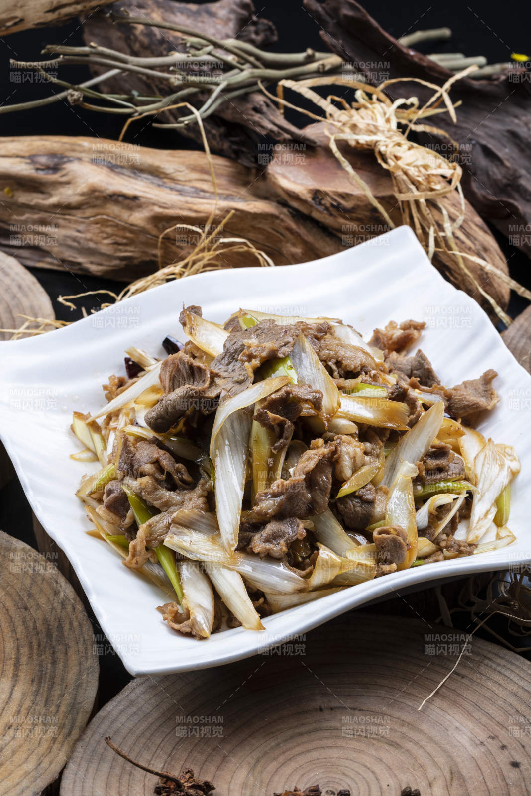 方形花瓷盘装的大葱爆羊肉摆放在樟木砧板上图片