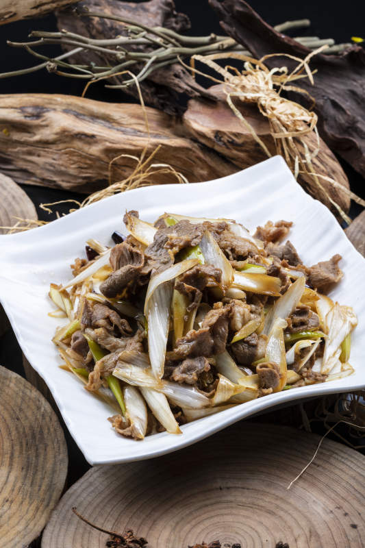 方形花瓷盘装的大葱爆羊肉摆放在樟木砧板上图片