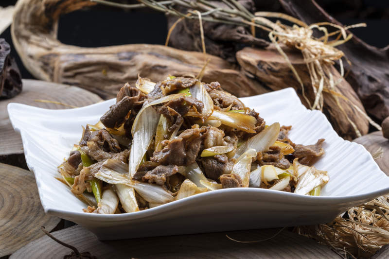 方形花瓷盘装的大葱爆羊肉摆放在樟木砧板上图片