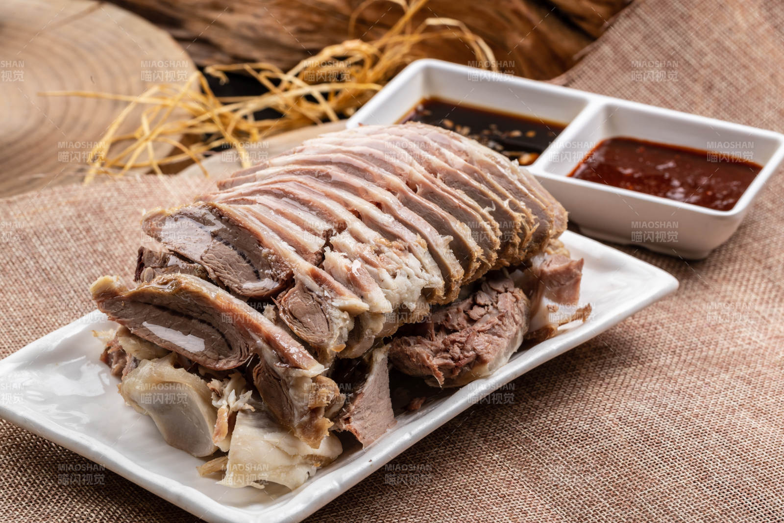 长方形瓷盘装的白灼羊背摆放在麻布垫子上图片