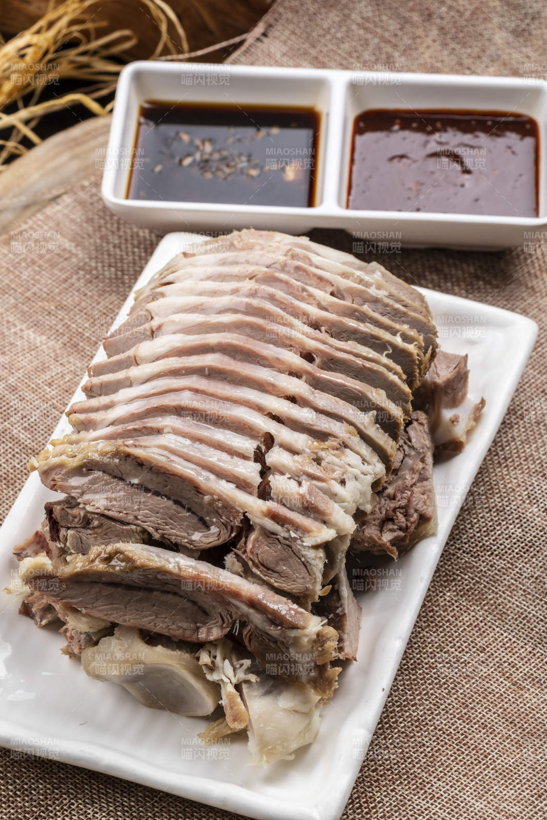 长方形瓷盘装的白灼羊背摆放在麻布垫子上图片