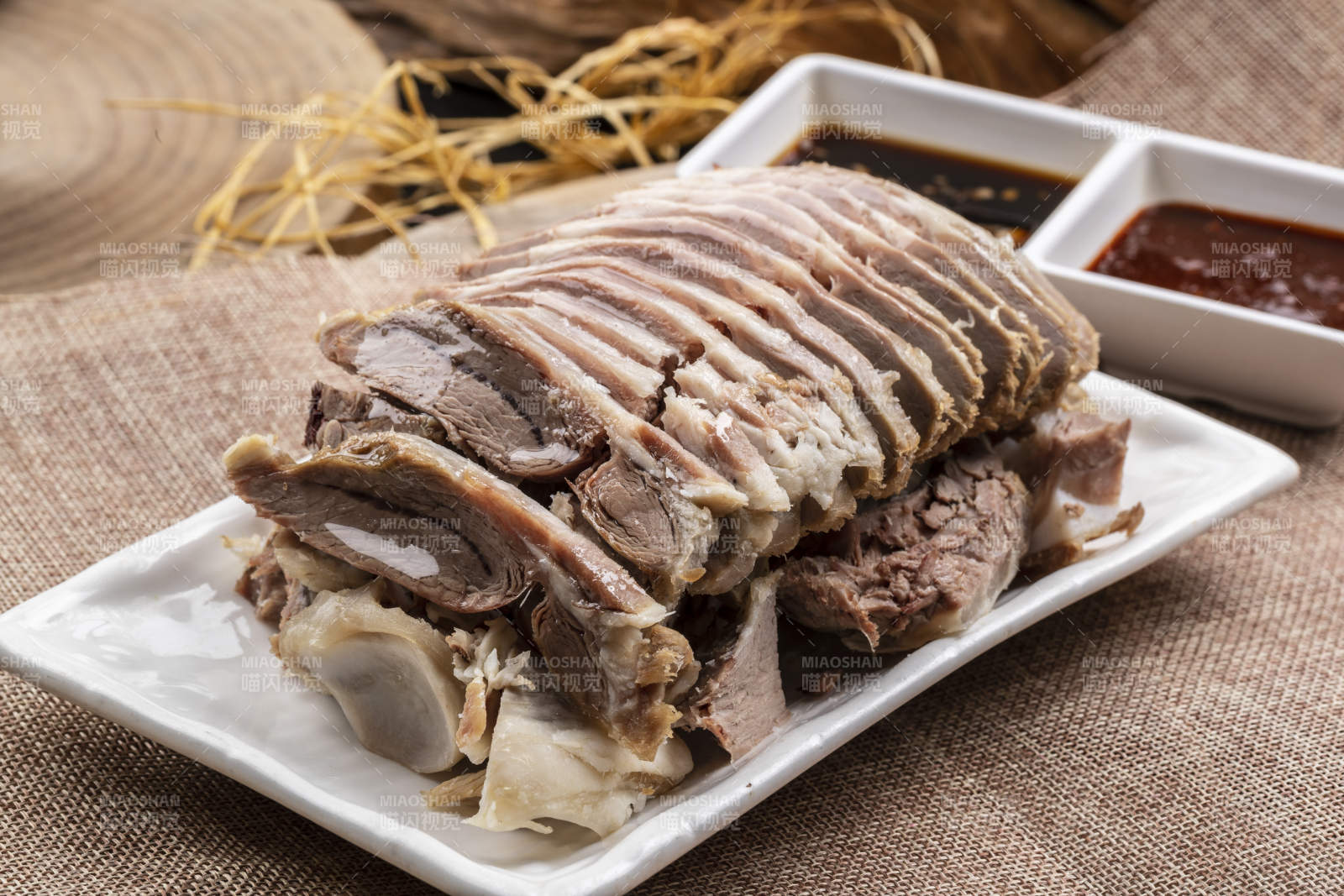 长方形瓷盘装的白灼羊背摆放在麻布垫子上图片
