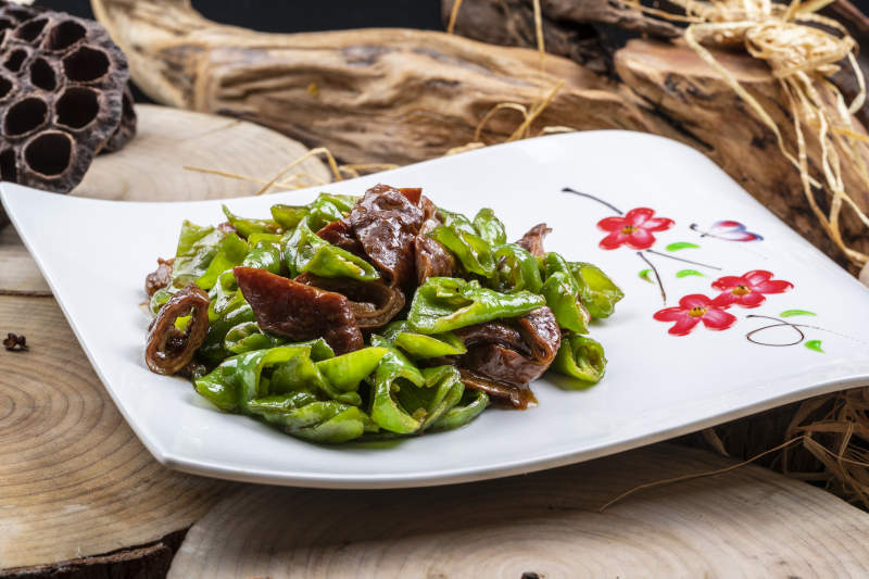 尖椒烧肥肠摆放在樟木砧板上图片