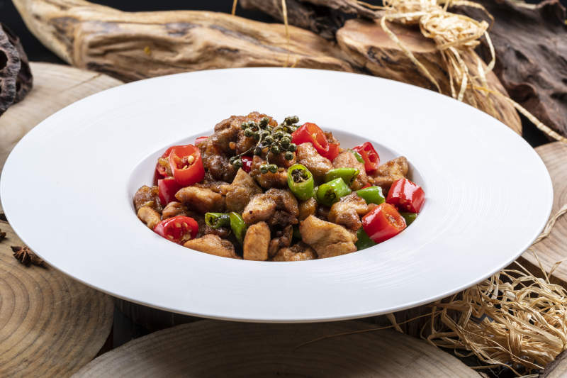 白色圆盘装的麻辣烧公鸡摆放在樟木砧板上图片