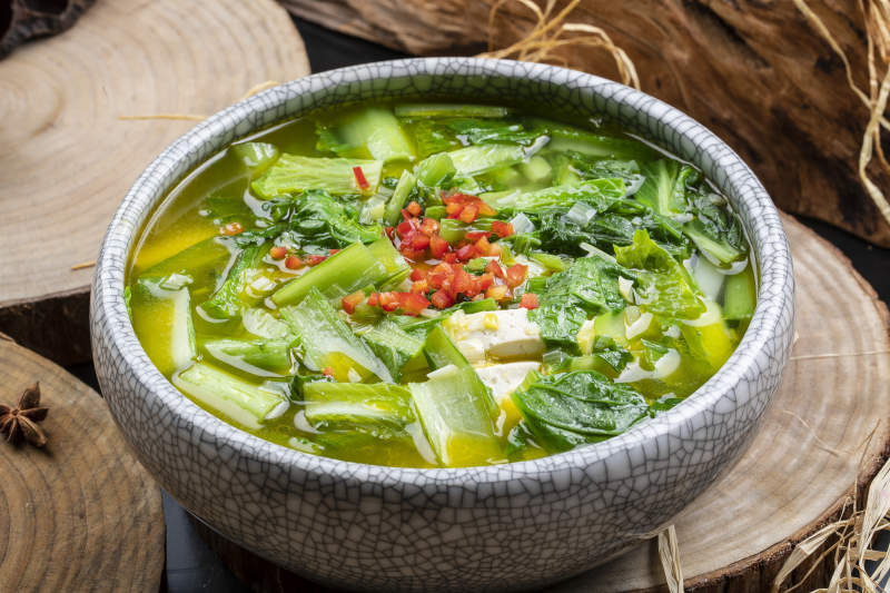 开片瓷碗装的小白菜烧豆腐摆放在樟木砧板上图片