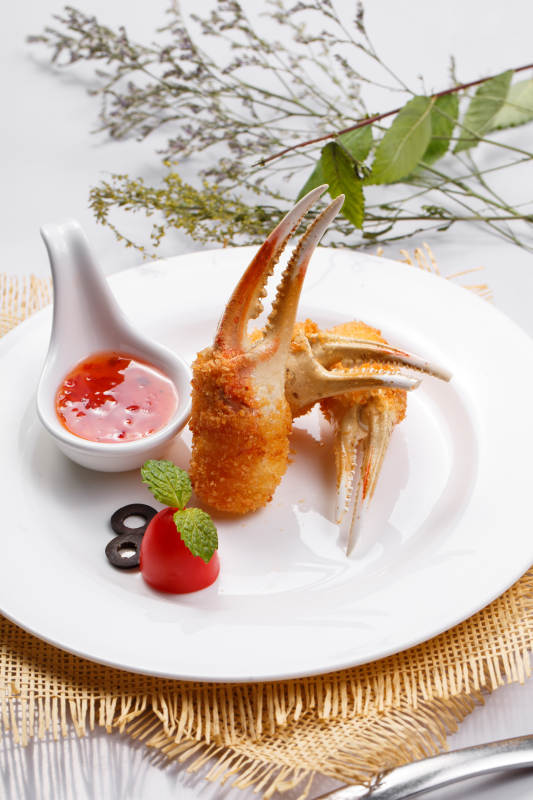 白色圆盘装面包糠芝士焗梭蟹钳摆放在草垫上图片