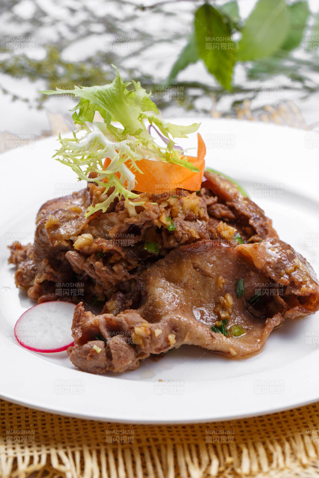 圆形白瓷盘装的铁板蒜香牛舌摆放在草垫上图片