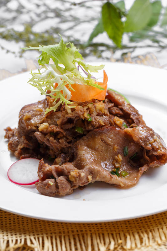 圆形白瓷盘装的铁板蒜香牛舌摆放在草垫上图片