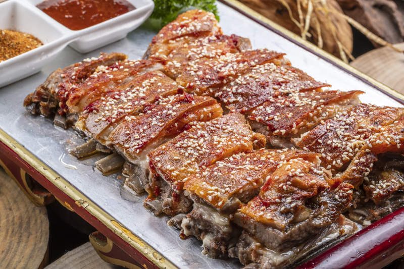 红色漆盘装的蒙古烤羊排摆放在樟木砧板上图片