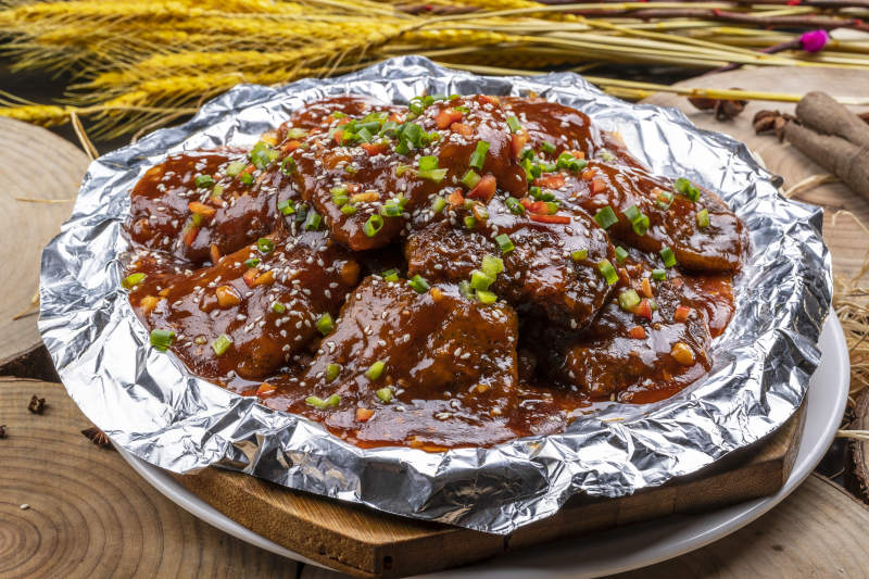 锡纸盘装的红烧脱骨带鱼摆放在樟木砧板上图片