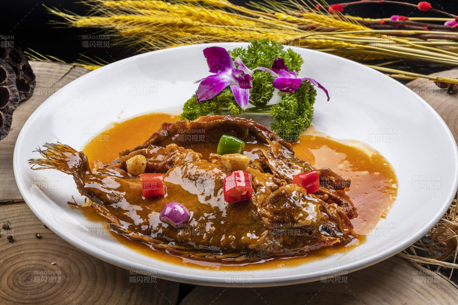 白色圆盘装的红烧罗非鱼摆放在樟木砧板上图片