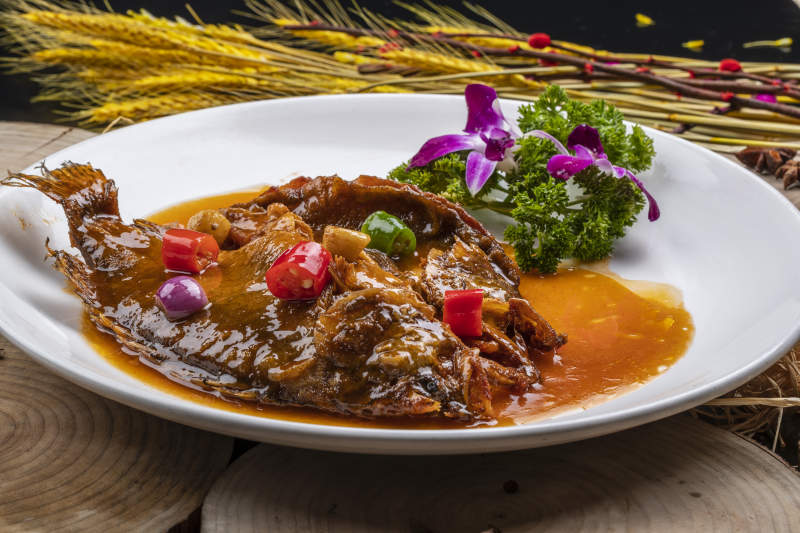 白色圆盘装的红烧罗非鱼摆放在樟木砧板上图片