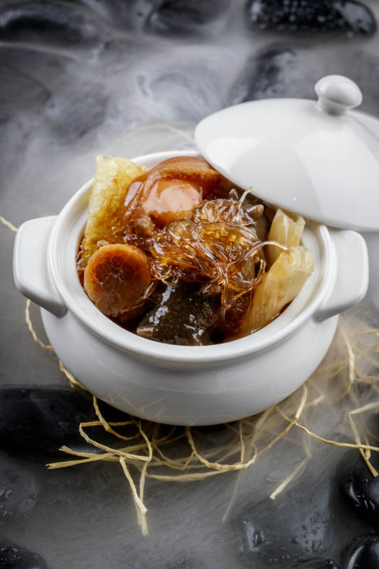 养生佛跳墙摆放在干冰缭绕的黑色鹅卵石山图片