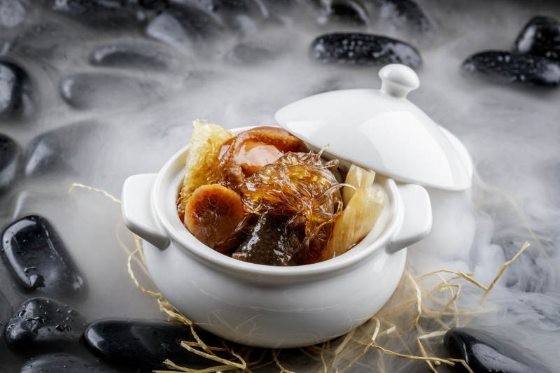 养生佛跳墙摆放在干冰缭绕的黑色鹅卵石山图片