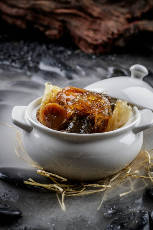 养生佛跳墙摆放在干冰缭绕的黑色鹅卵石山图片