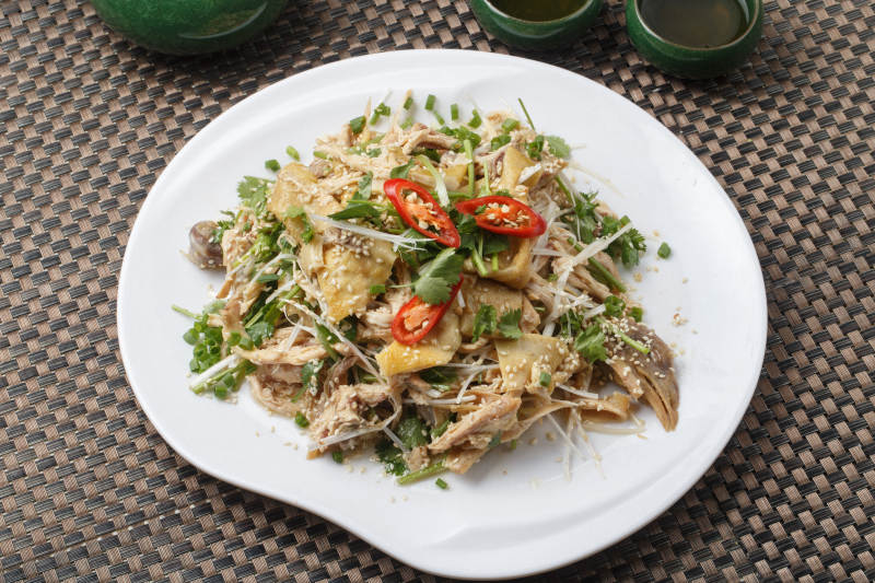 扇形白瓷盘装的麻辣手撕鸡摆放在餐垫上图片