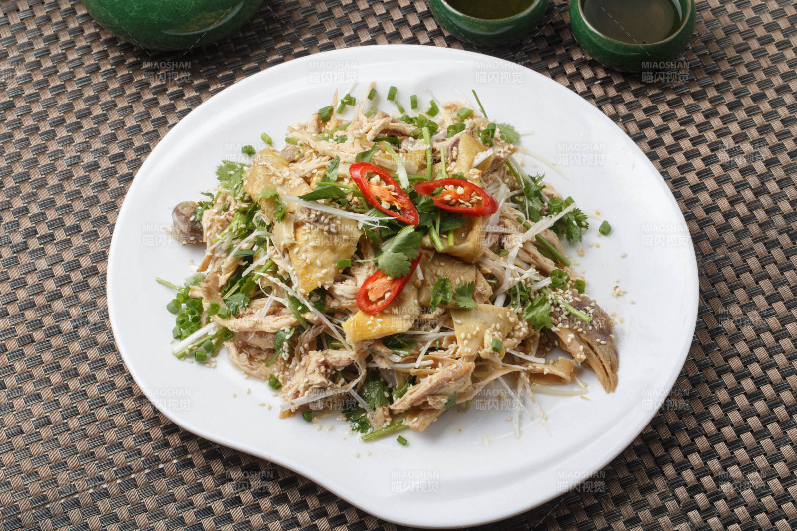 扇形白瓷盘装的麻辣手撕鸡摆放在餐垫上图片