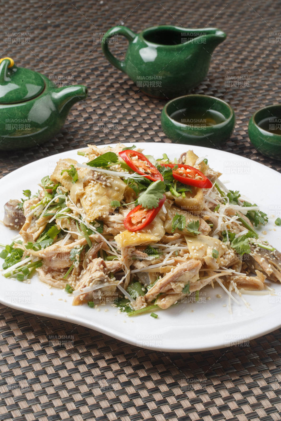 扇形白瓷盘装的麻辣手撕鸡摆放在餐垫上图片