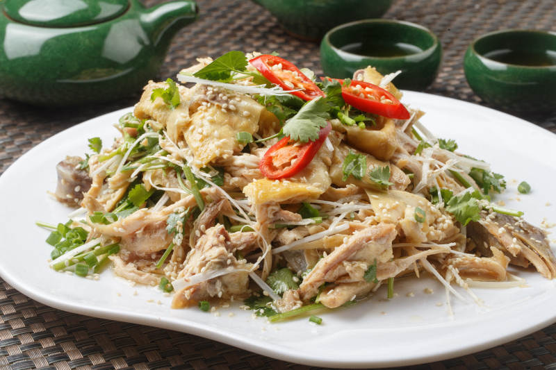 扇形白瓷盘装的麻辣手撕鸡摆放在餐垫上图片