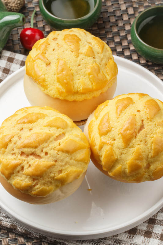 圆形白瓷盘装的酥皮菠萝包摆放在餐垫上图片