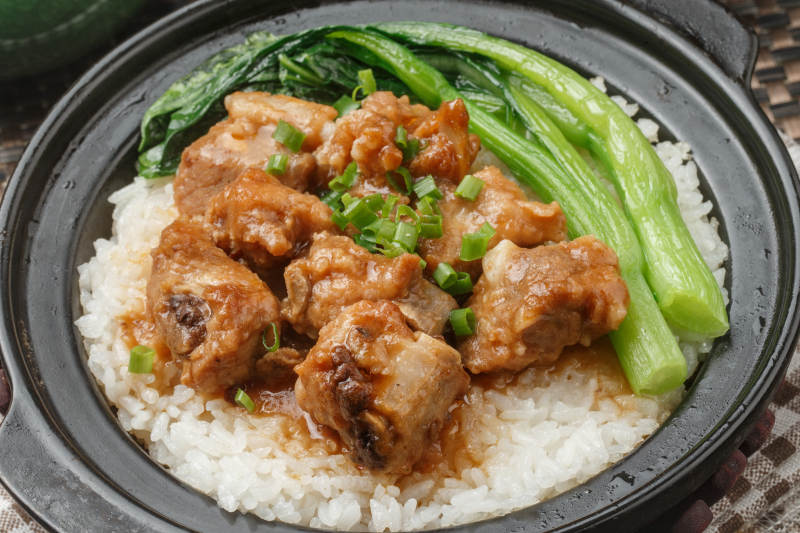黑色砂锅装的排骨芥蓝煲仔饭摆放在餐布上图片