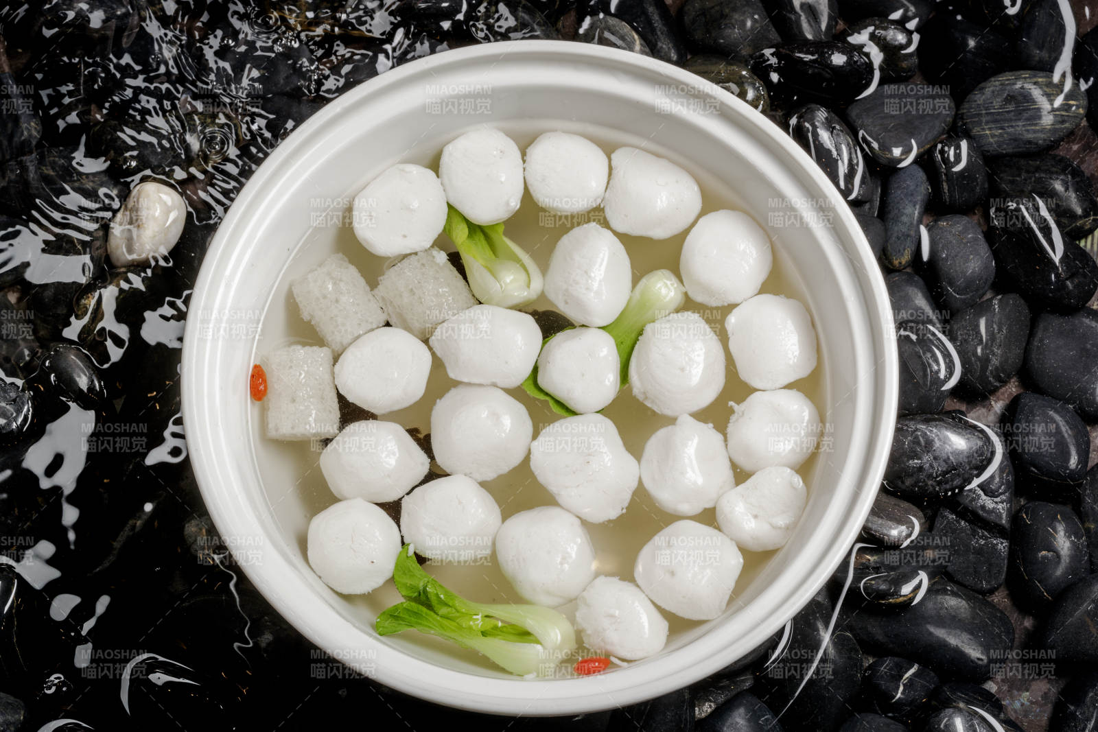 西湖鱼圆摆放在布满黑色鹅卵石的水中图片