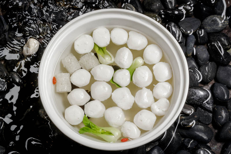 西湖鱼圆摆放在布满黑色鹅卵石的水中图片