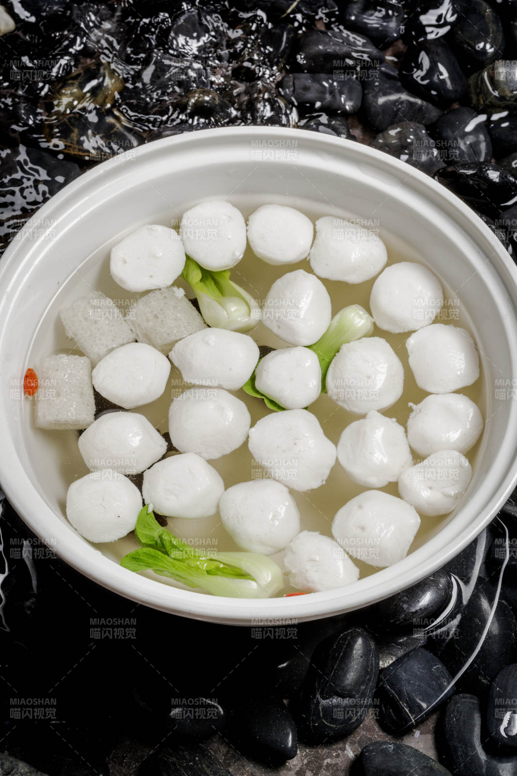 西湖鱼圆摆放在布满黑色鹅卵石的水中图片