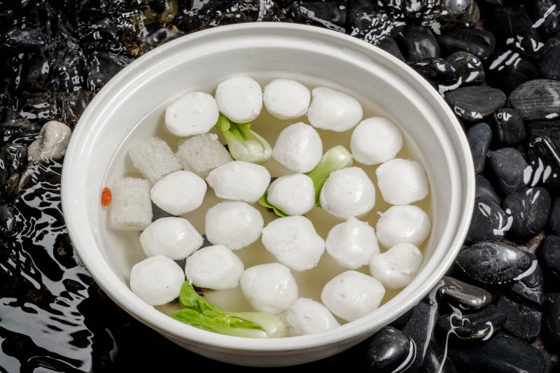 西湖鱼圆摆放在布满黑色鹅卵石的水中图片