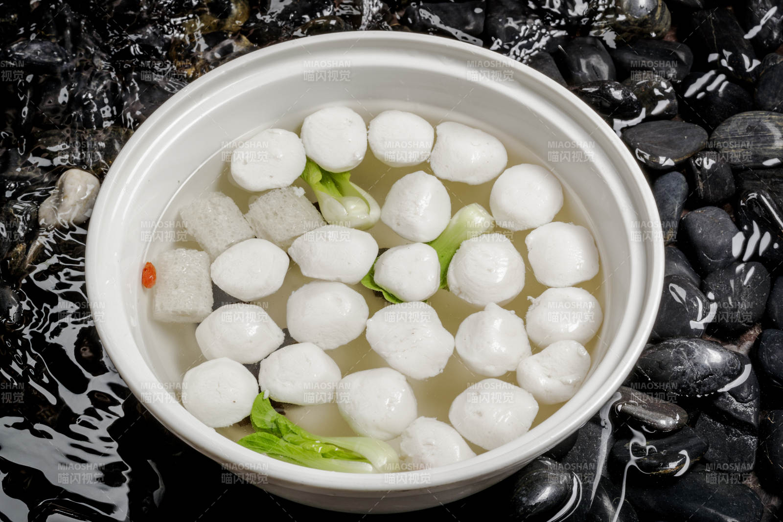 西湖鱼圆摆放在布满黑色鹅卵石的水中图片