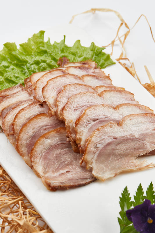 白色瓷盘装的烟熏猪肘五花肉图片